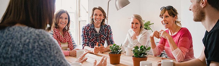 Erwachsene Personen sitzen um einen Tisch herum und unterhalten sich angeregt.